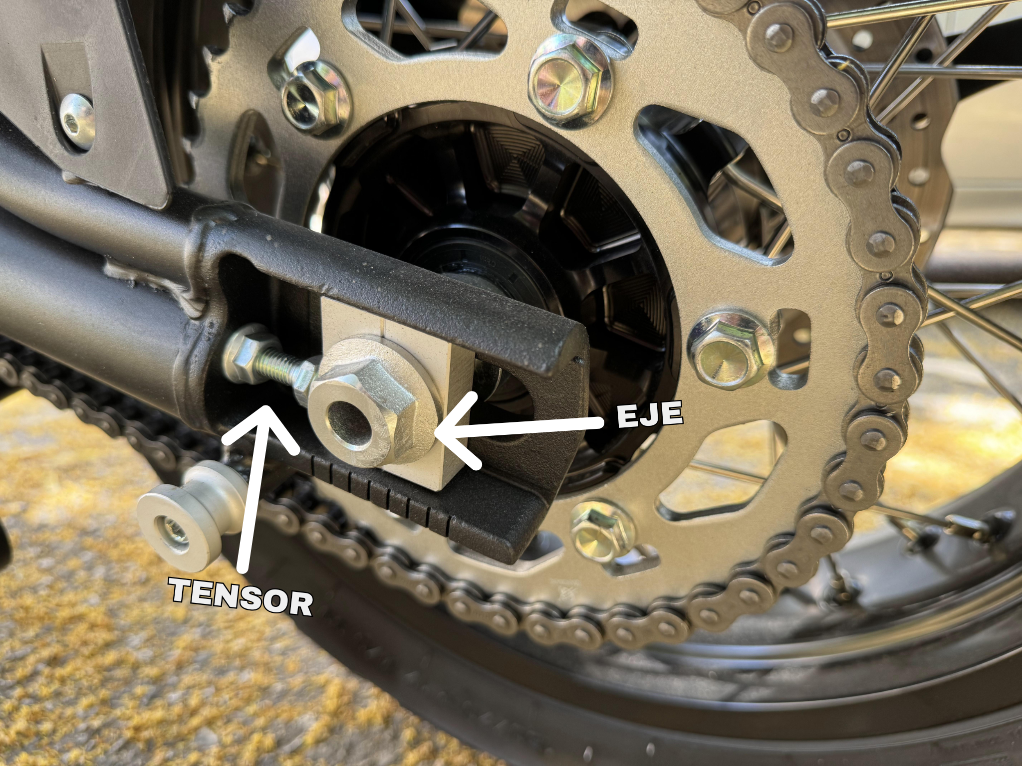 Tensor de cadena y eje trasero de moto con flechas indicativas